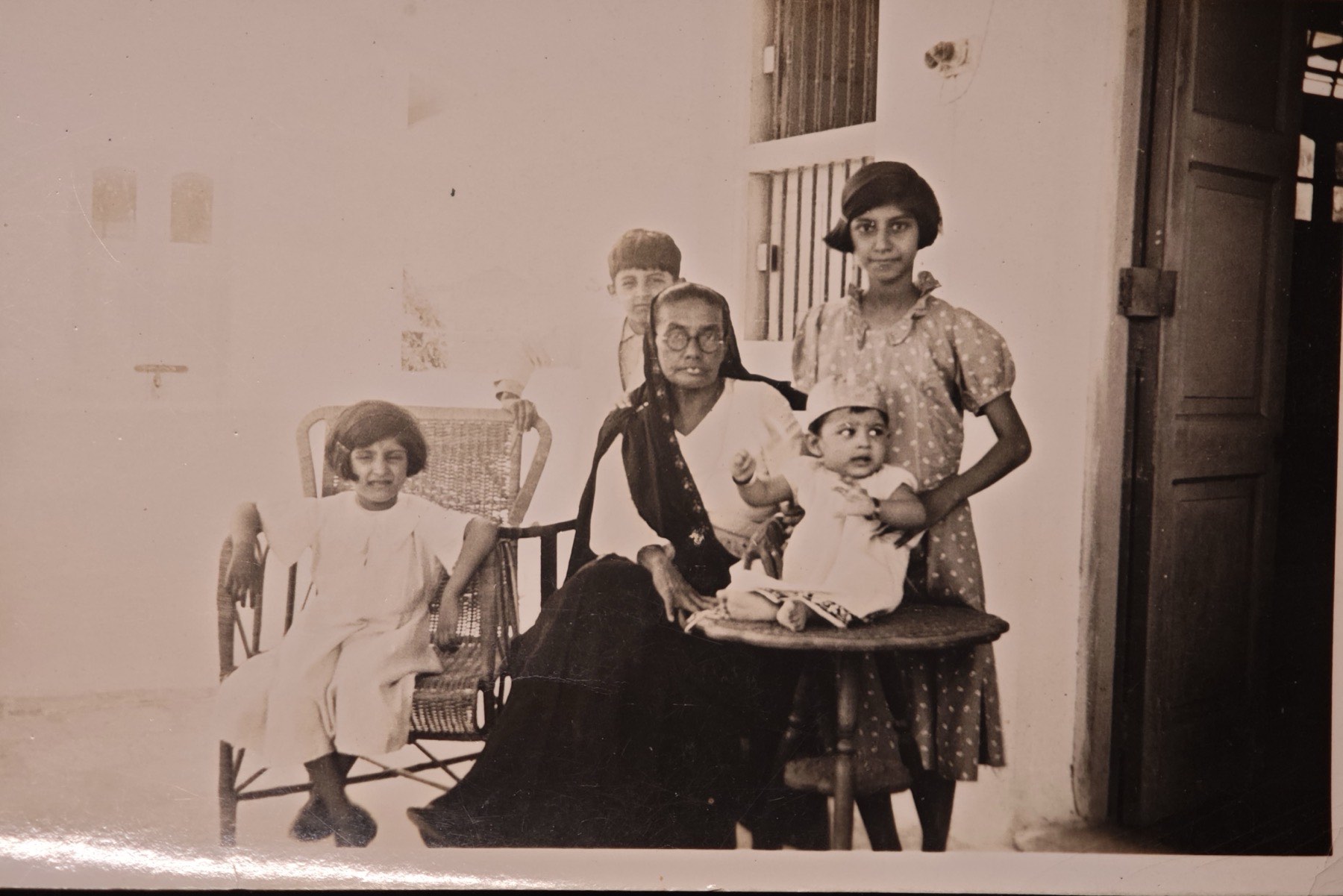 Jerbai Daroga, in a dark sari, seated on a veranda with her grandchildren around her and a baby on her lap.