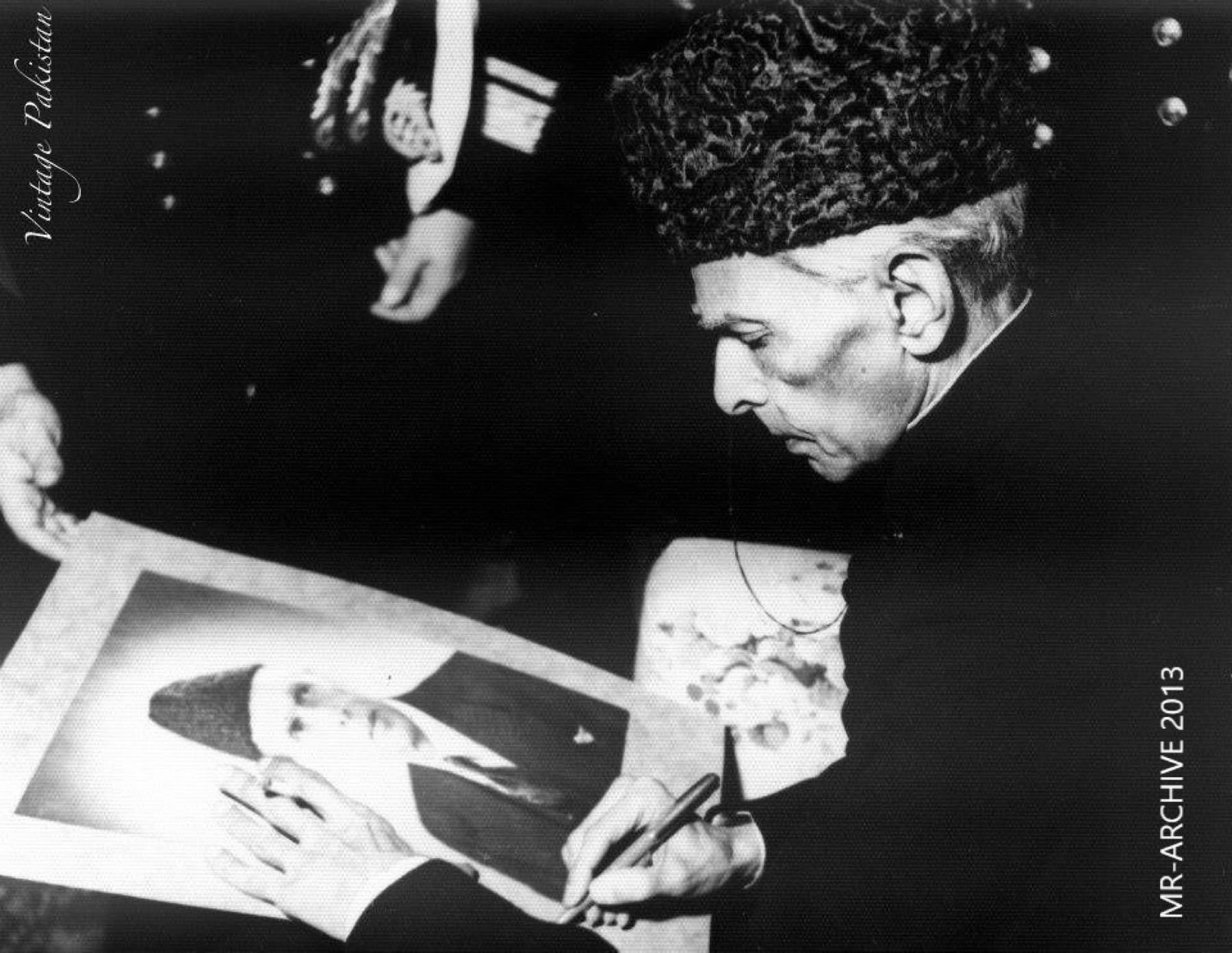 Muhammad Ali Jinnah, in a karakul cap, signing a print of his official portrait.