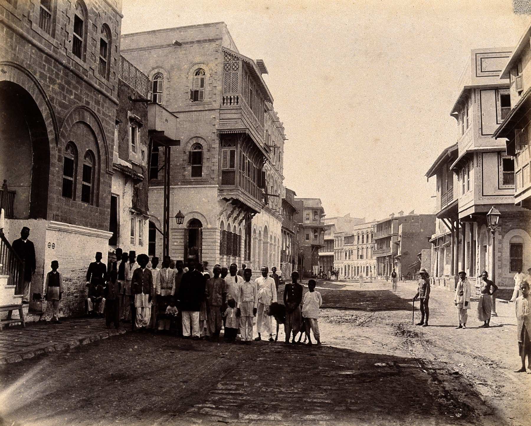 Rampart Row in Mithadar, Old Karachi, in 1897: tall stone buildings with wooden balconies, and a group of people standing in the street.