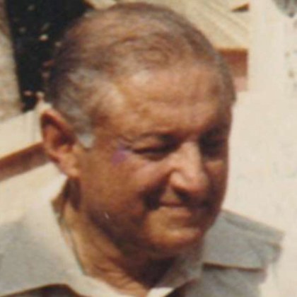 Sam in later life: an older man with thinning grey hair swept back, smiling and looking down.